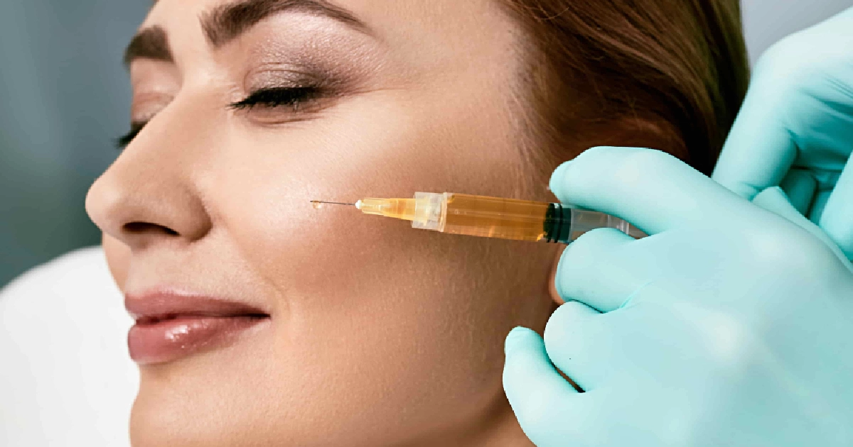 A woman receives PRP Facials in Greensboro, NC, smiling with eyes closed as a gloved professional injects her cheek with a yellow serum.